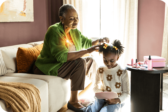 Adult helping a child with their hair while the child looks at a book
