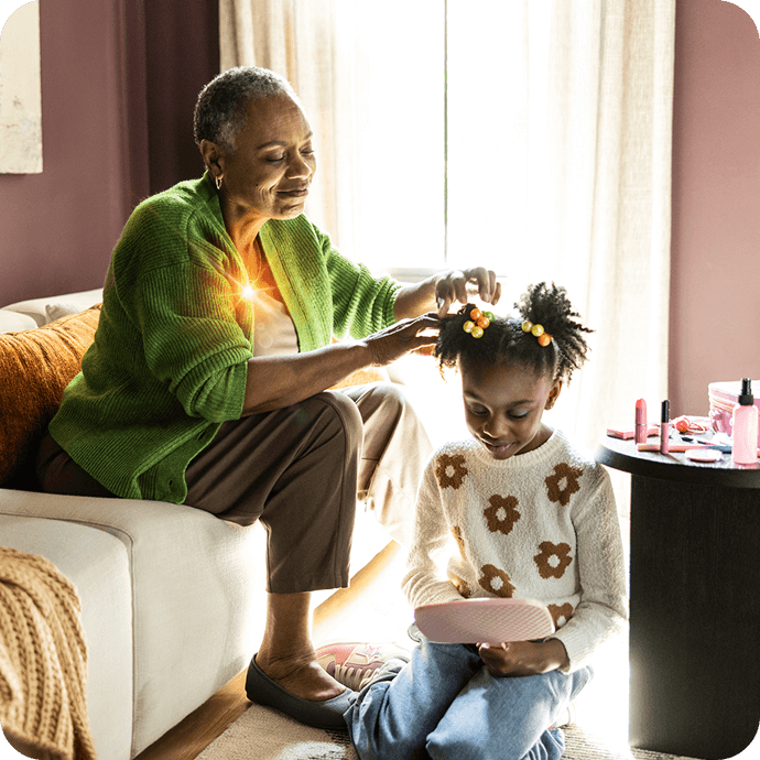 Adult helping a child with their hair while the child looks at a book
