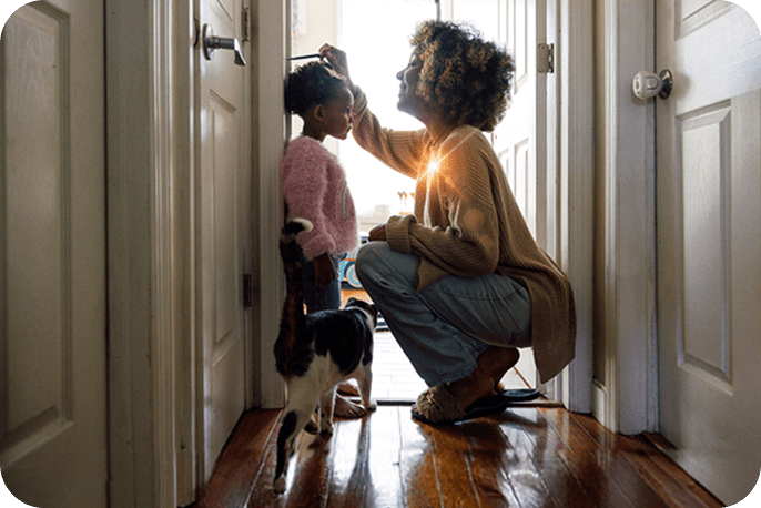 Adult kneeling to measure a child’s height in a hallway at home