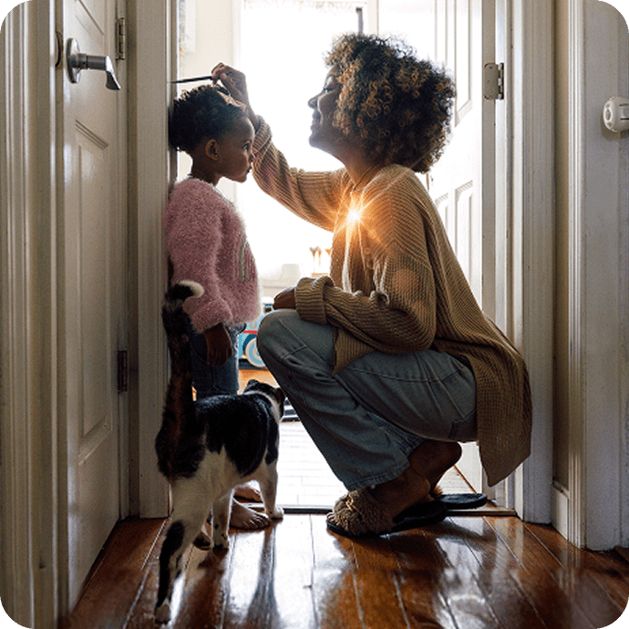 Adult kneeling to measure a child’s height in a hallway at home